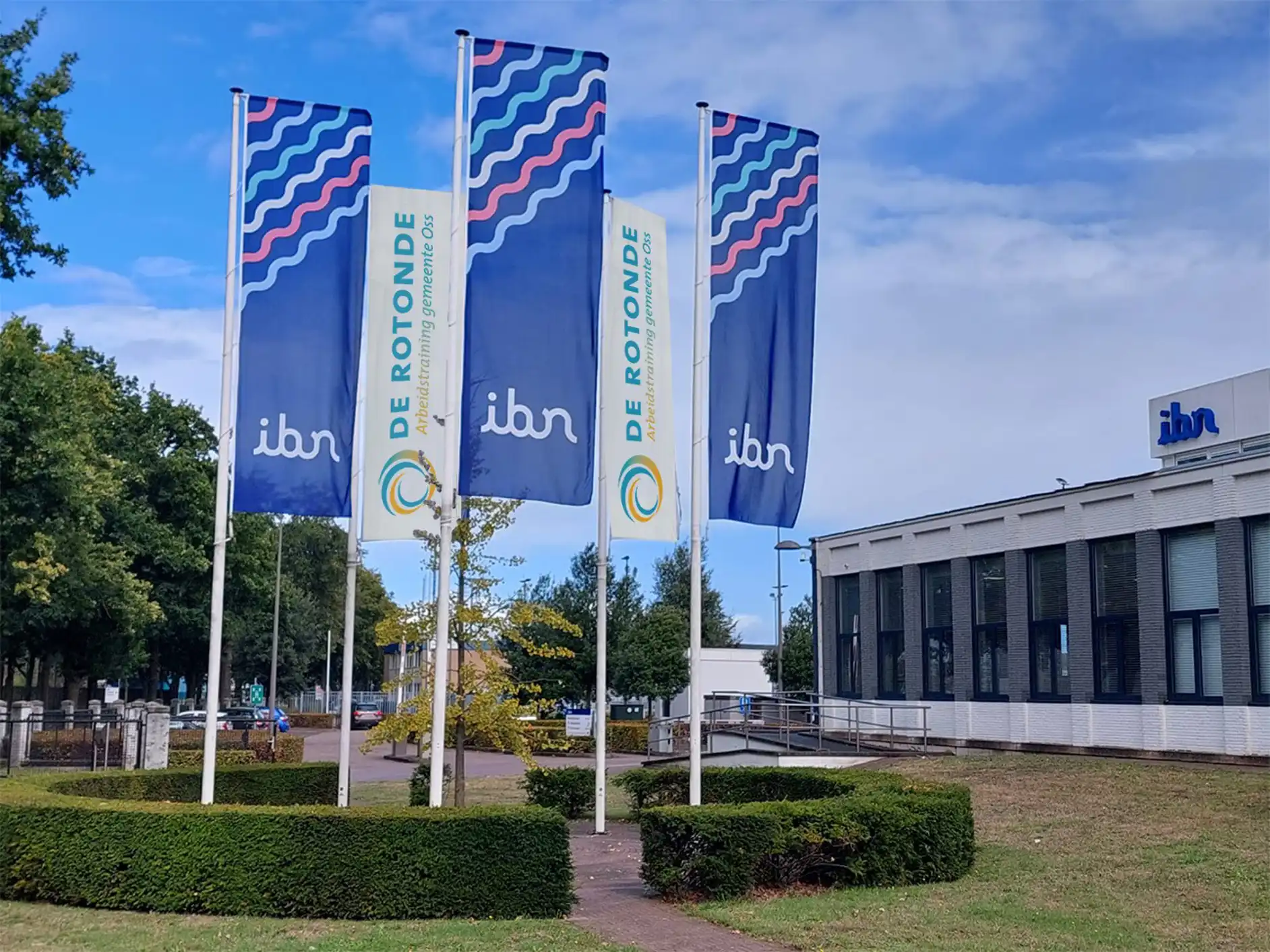 Vlaggen van de Rotonde en IBN wapperen samen bij het pand van IBN in Oss.