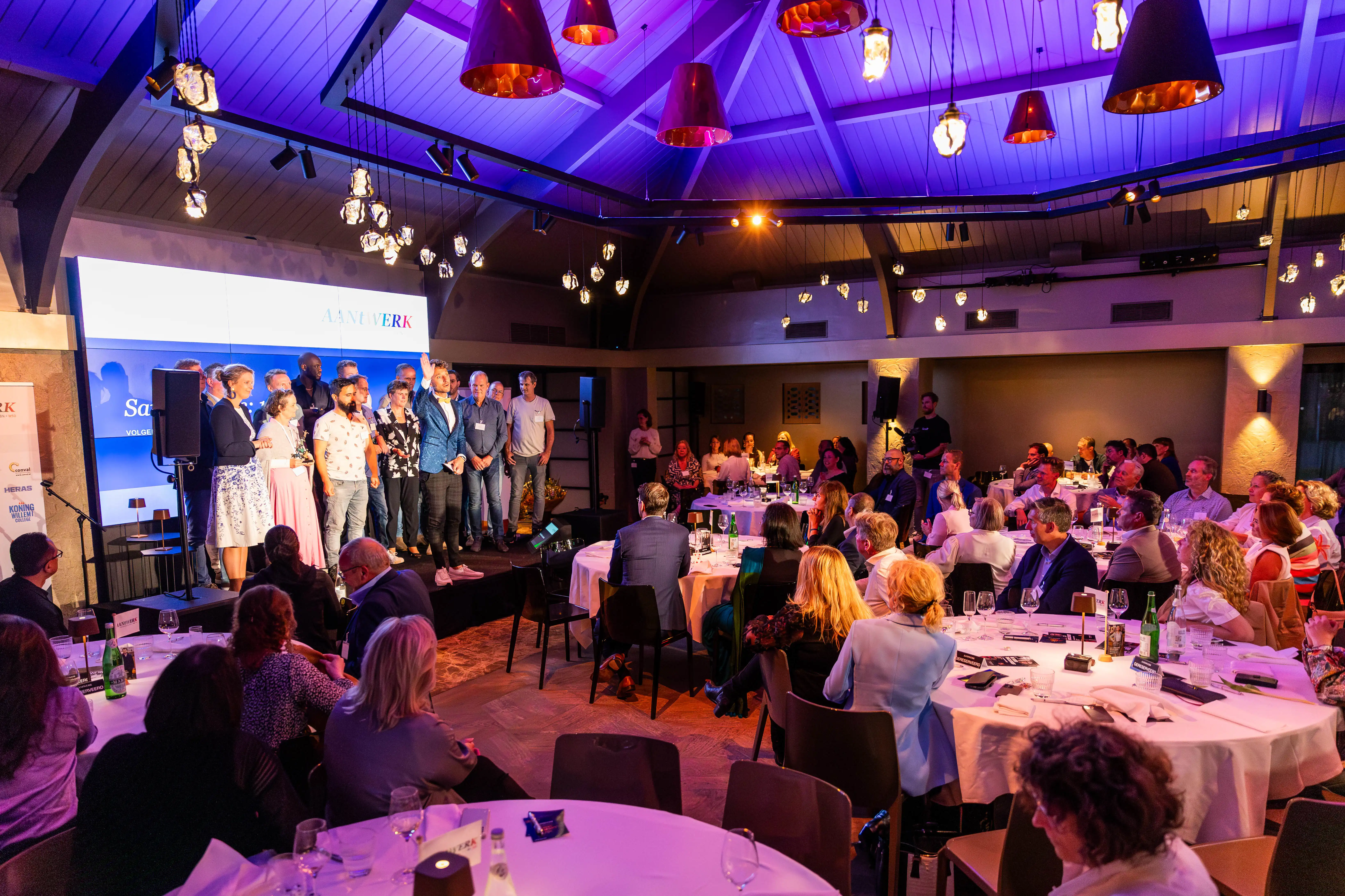 Overzichtsfoto van de zaal met daarop het podium met de presentator