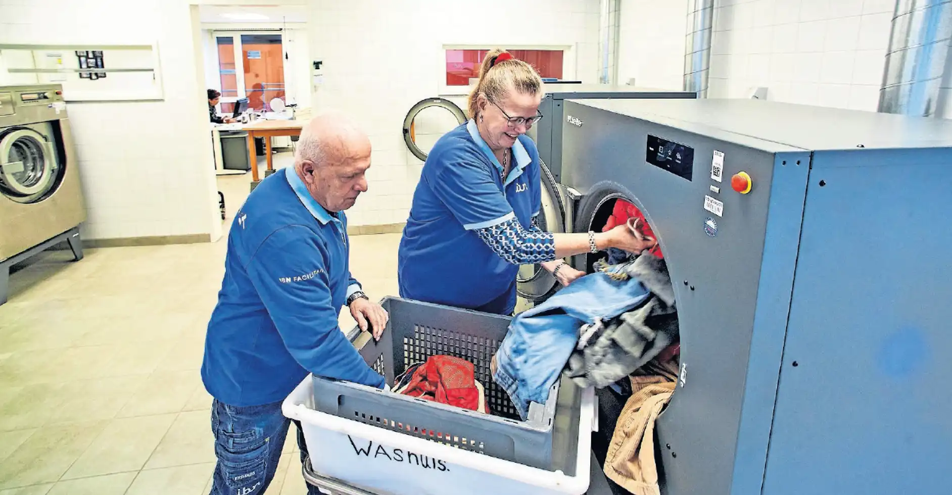 Foto van twee IBN medewerkers die de was in het machine doen
